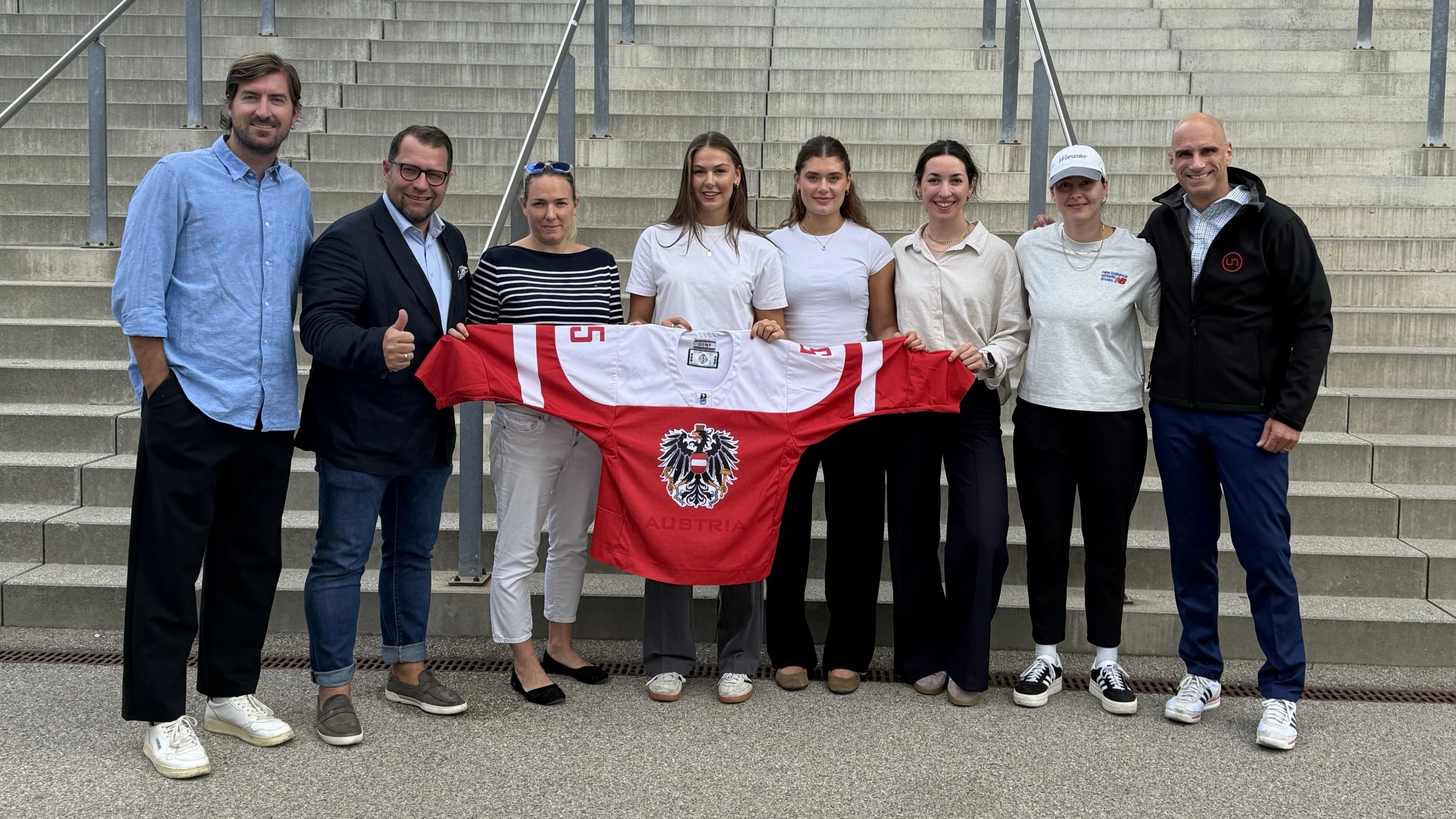 Vertreter:innen des ÖEHV und Spielerinnen des Frauen-Nationalteams stehen gemeinsam vor einer Stiege und halten ein rot-weißes Österreich-Trikot mit der Nummer 5 in die Kamera.