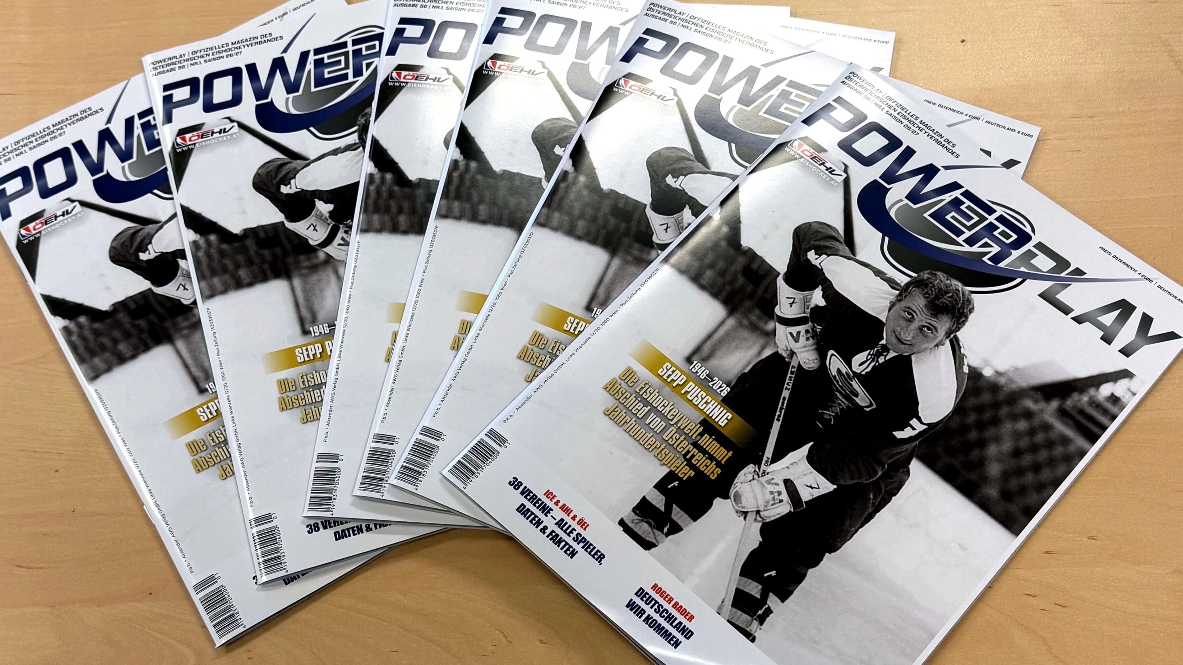 Mehrere Exemplare des Eishockey-Magazins Powerplay (Ausgabe 56) liegen fächerförmig auf einem Holztisch. Das Cover zeigt ein Schwarz-Weiß-Foto von Sepp Puschnig im KAC-Trikot mit der Nummer 7 beim Schlagschuss, dazu die Schlagzeilen „Sepp Puschnig 1946–2026 – Die Eishockeywelt nimmt Abschied von Österreichs Jahrhundertspieler", „38 Vereine – alle Spieler, Daten & Fakten" und „Roger Bader: Deutschland, wir kommen".
