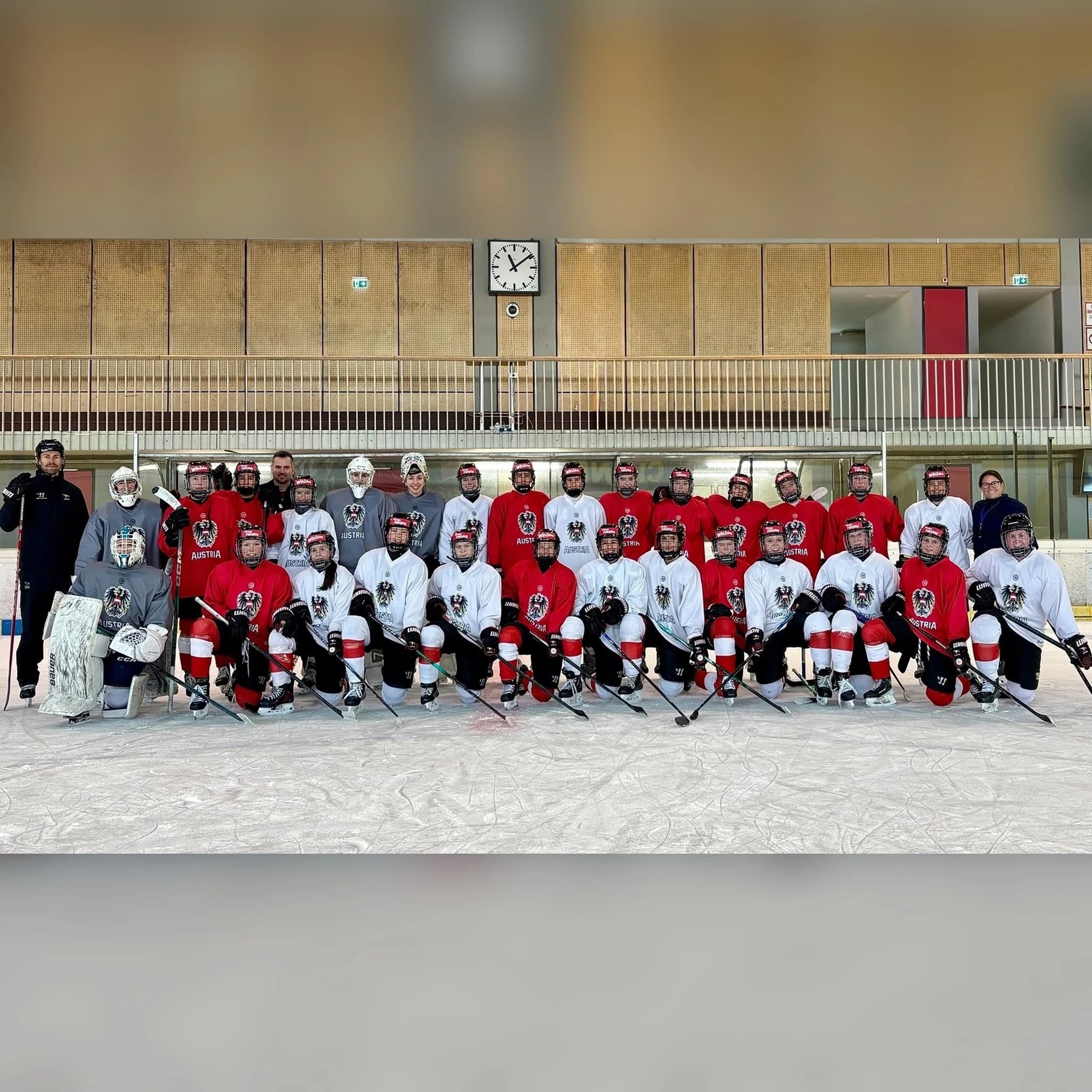 Gruppenfoto des österreichischen Frauen-Nationalteams beim Lehrgang in Klagenfurt: Die Spielerinnen in roten, weißen und grauen Trainingstrikots mit Bundesadler und „Austria“-Schriftzug knien und stehen in zwei Reihen auf dem Eis, flankiert von Betreuerinnen und Betreuern des Trainerteams.